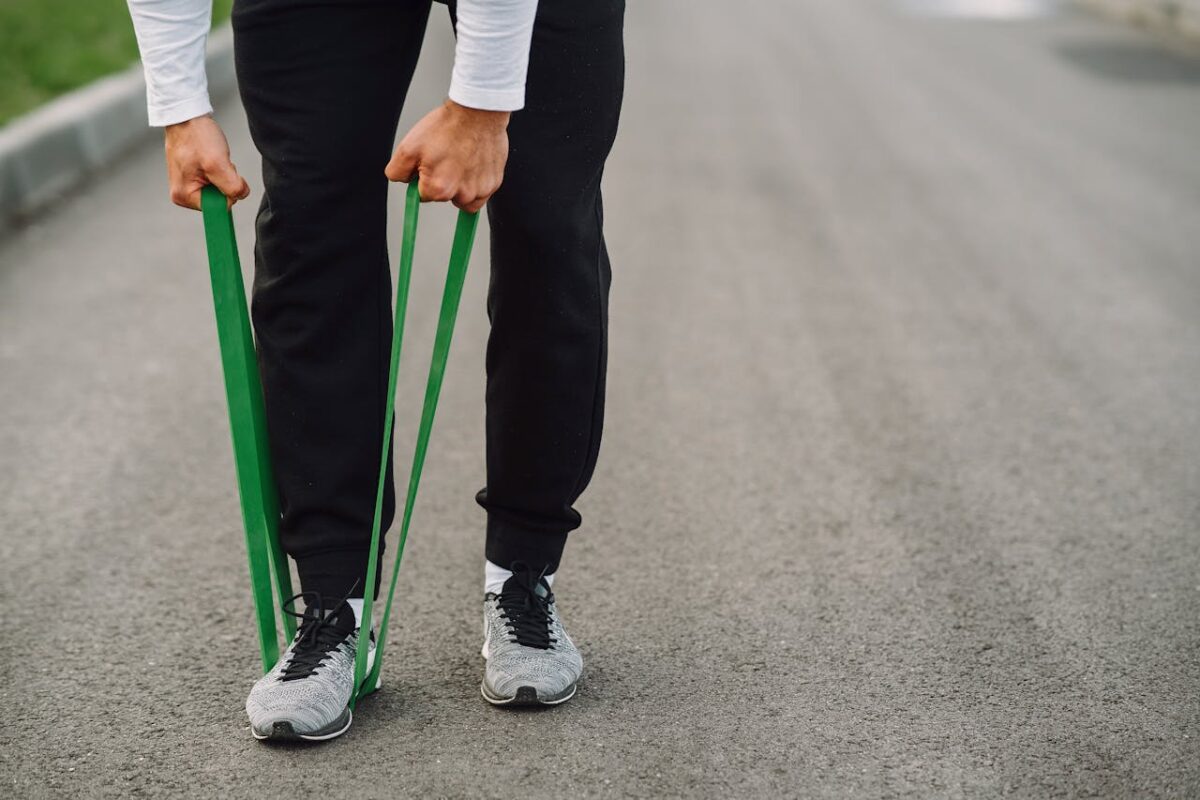 who-we-are An athlete uses green resistance bands for a workout on a paved path.