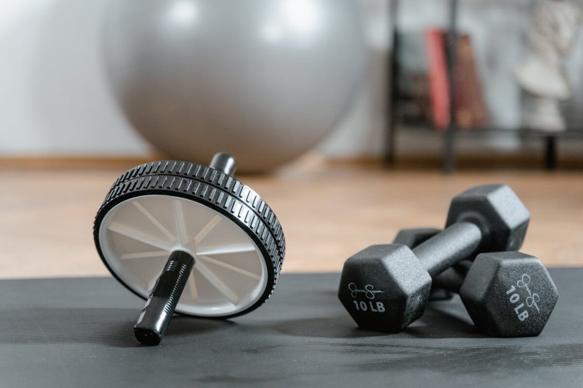 Close-up of ab wheel and dumbbells on a mat in a home gym setting.