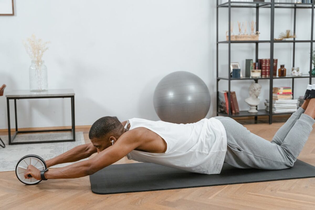Man using an ab roller on a yoga mat indoors, promoting fitness and healthy lifestyle.